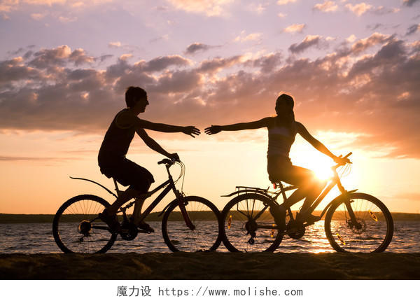 年轻夫妇年轻情侣在海边日落骑自行车运动锻炼幸福情侣